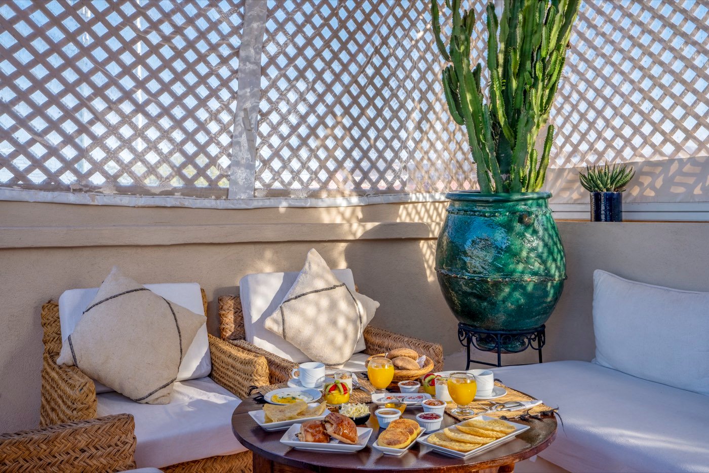 Breakfast laid out on a low table on the roof terrace — pastries, msemen, orange juice and coffee, beside a glazed green urn