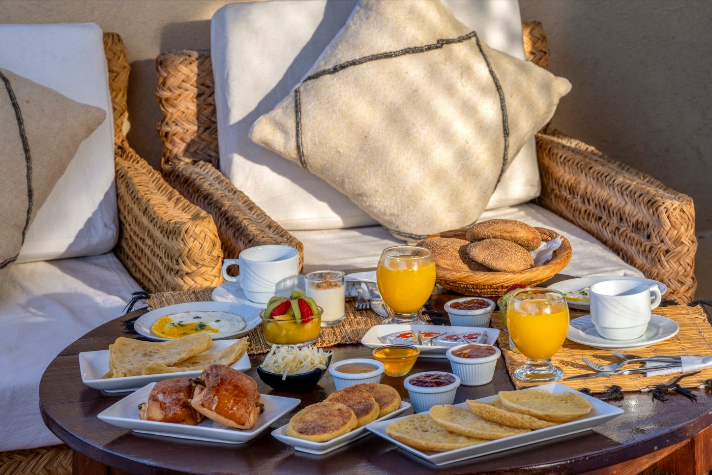Msemen and beghrir stacked on white plates, with pastries, preserves and coffee alongside