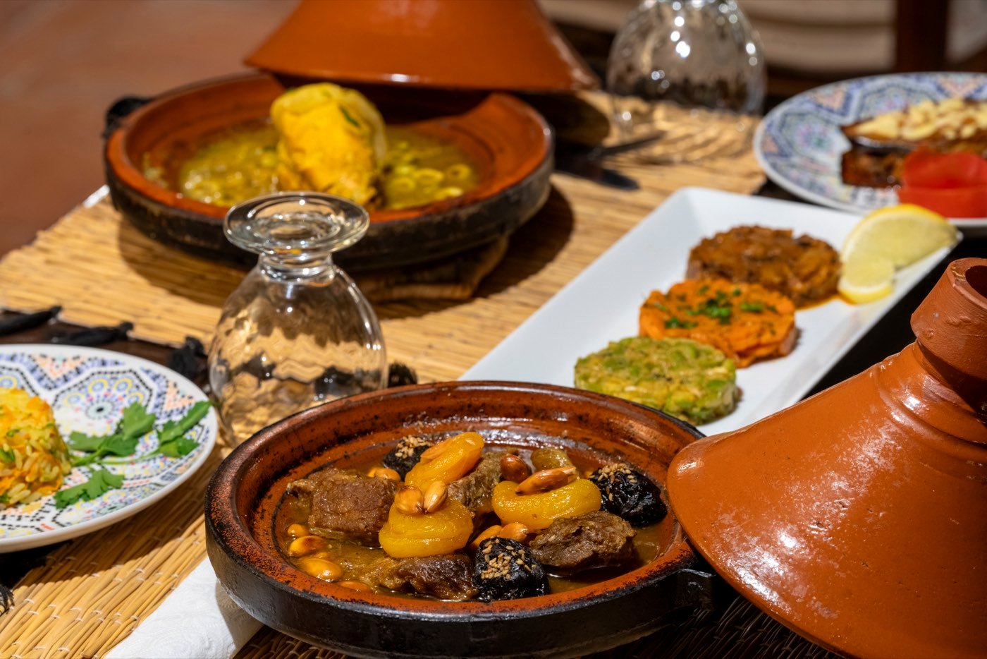 A lamb tajine with apricots, prunes and pine nuts, beside a plate of cooked salads and a second tajine still under its lid