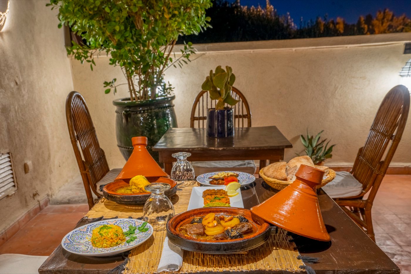 A table on the terrace at night, two tajines set out with bread and saffron rice under the trees
