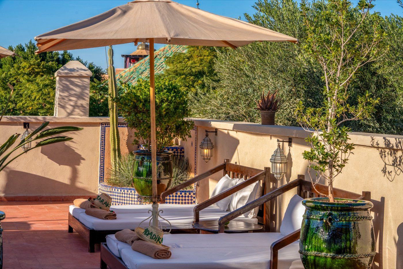 Rooftop daybeds under a canvas parasol beside a glazed green urn