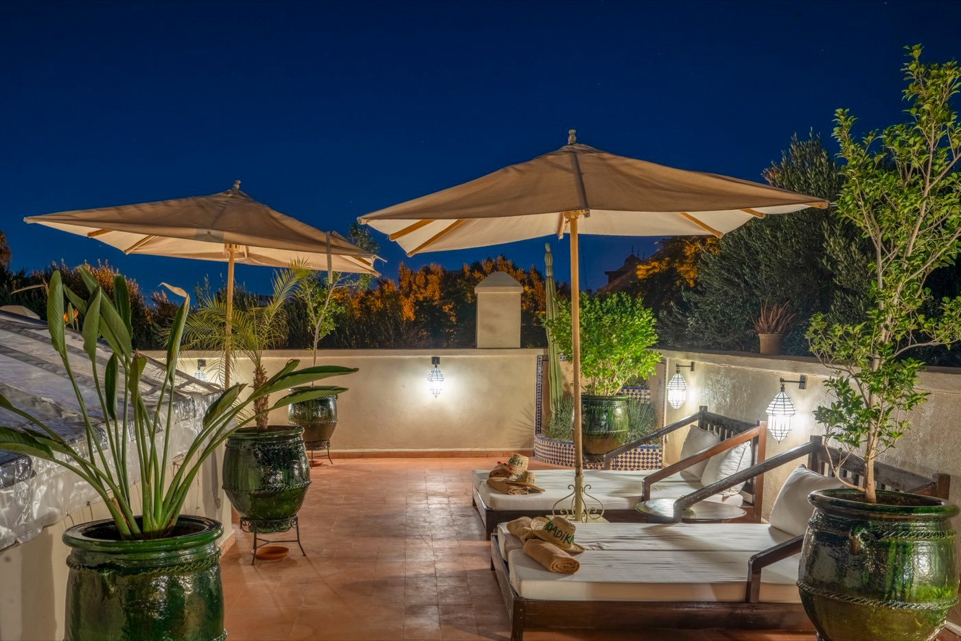 The rooftop after dark, parasols and daybeds under a deep blue sky