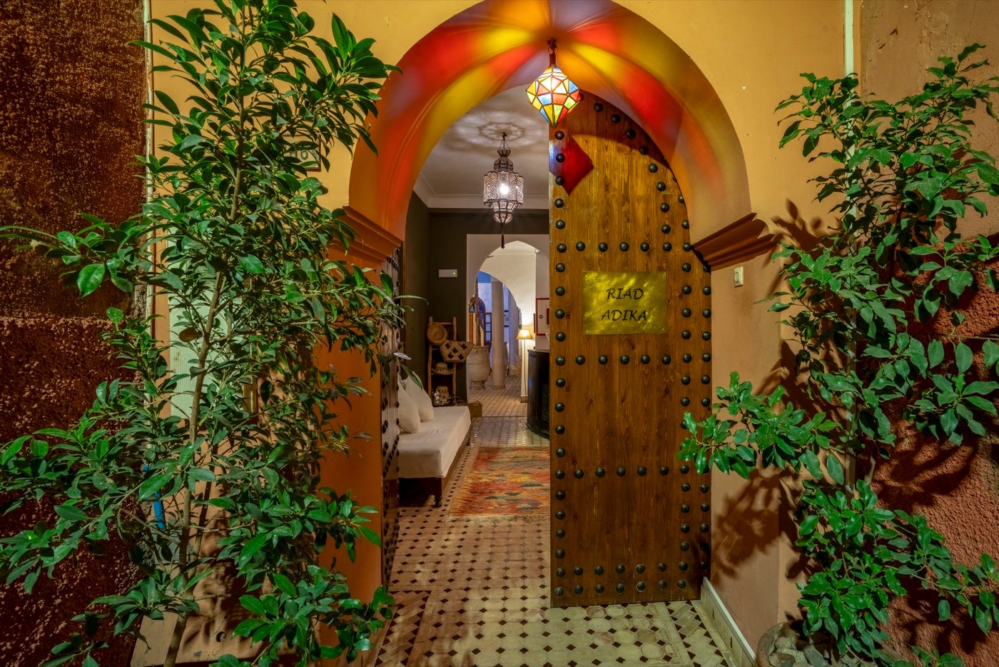 The carved entrance door of Riad Adika, framed by a painted arch and potted greenery