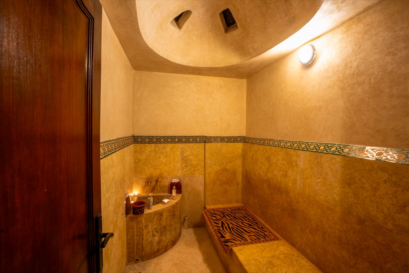 The domed steam room of the hammam, its heated stone bench lit by candles beneath a band of zellige