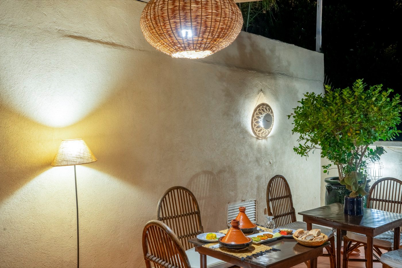 The terrace after dark, lit by a woven pendant lamp, a tajine waiting on the table below