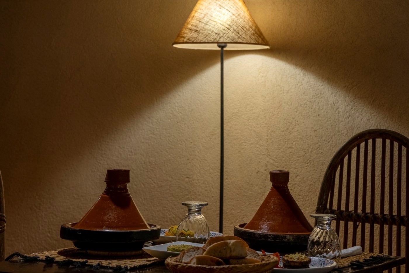 Two tajines under a standing lamp, bread and olives between them