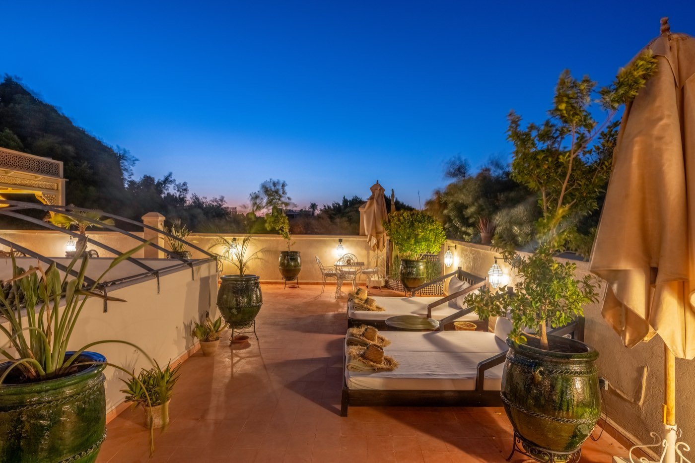 Daybeds along the upper terrace at dusk, parasols furled and planted urns against the wall