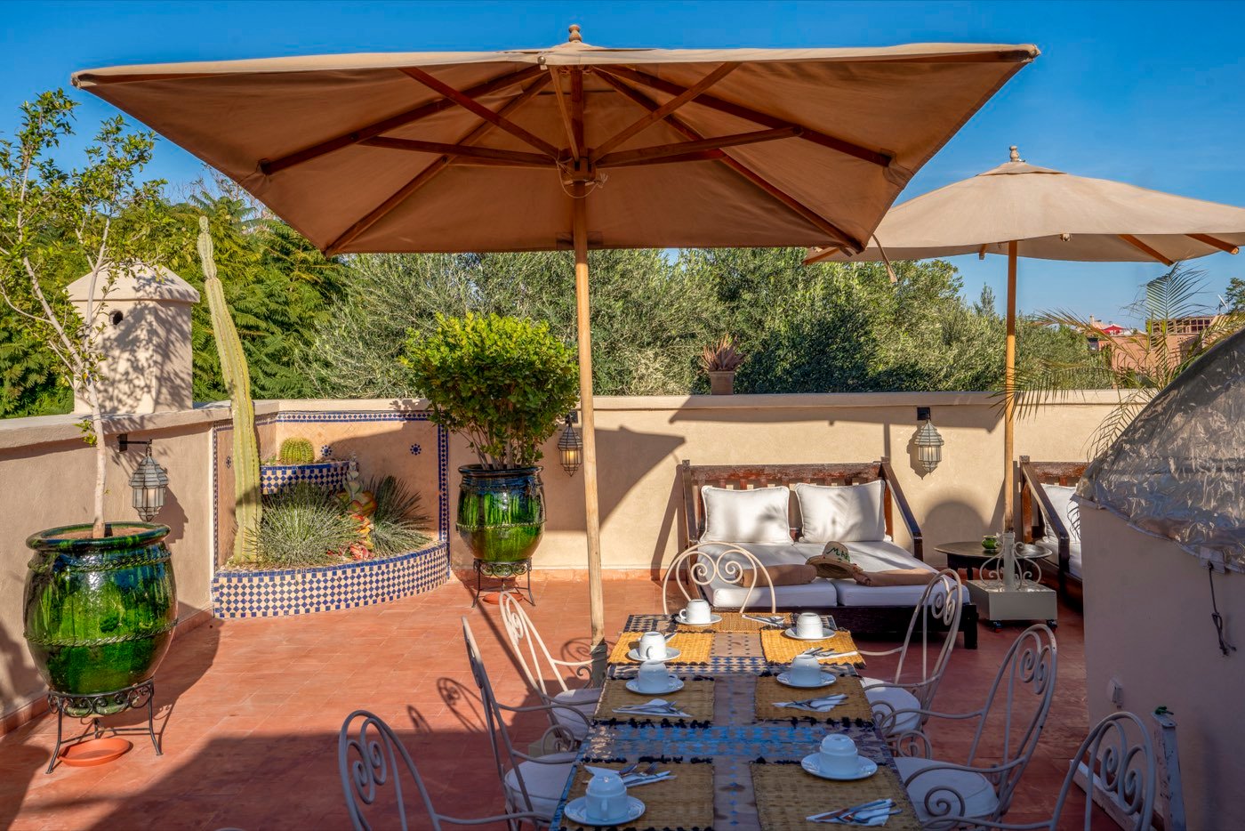 A long table laid on the roof terrace under canvas parasols, olive trees and the medina beyond
